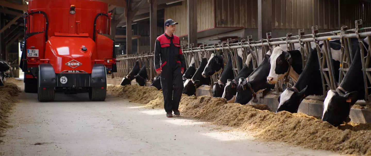 éleveur dans l'étable avec mélangeuse automotrice à l'arrière plan